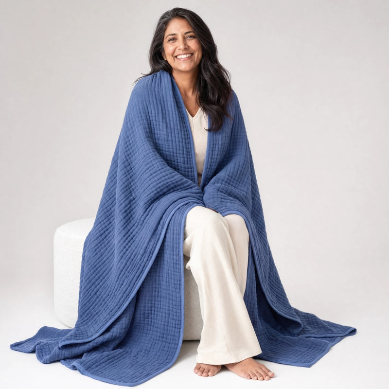 Woman on a pouf with the Koforto Muslin Blanket in sand draped to the floor