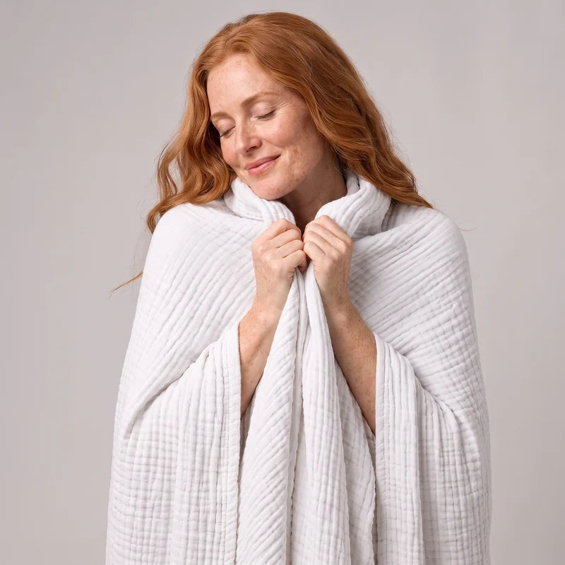 Woman wrapped head to toe in the Koforto Muslin Blanket in sand